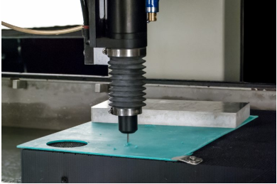 A drill attachment on an Omax waterjet. Note the simple fixturing, all that’s needed for the abrasive jet to cut edges and enlarge holes.